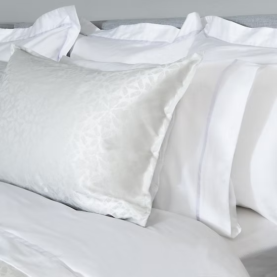 White satin Aura Jacquard Shams on a bed with a neutral background