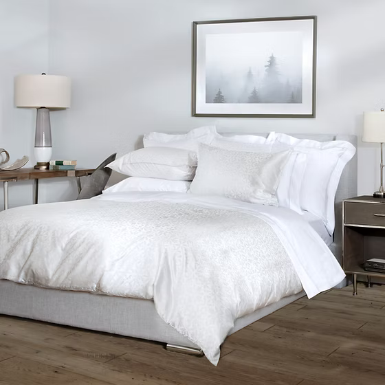 Neatly made bed with white Aura | Jacquard Duvet & Shams in a bedroom setting.