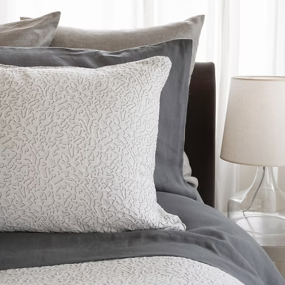 Textured pillows from Athena Jacquard Duvet Cover Set on a bed with a lamp in the background