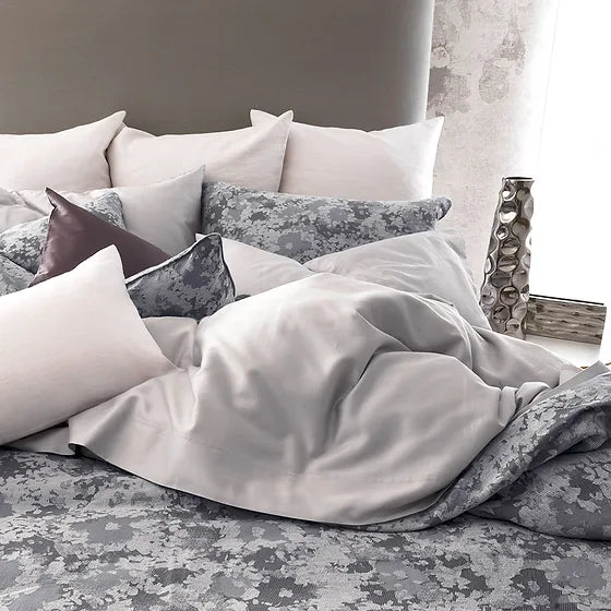 A bed with Sakura jacquard bedding in a gray floral pattern, with a duvet cover and multiple pillows arranged on the bed.
