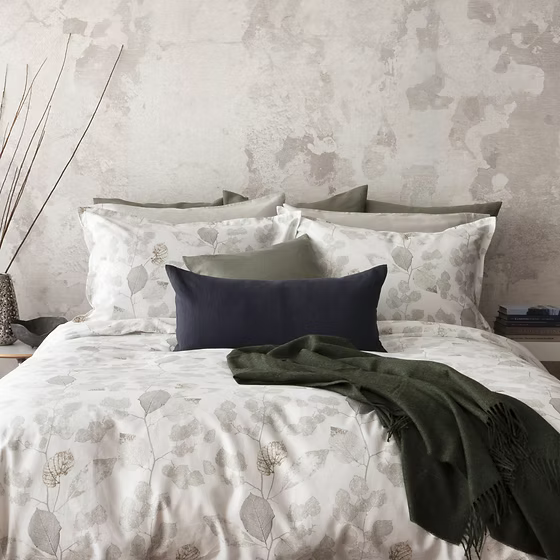 Bed with floral Aspen printed sateen bedding and pillows against a textured wall.