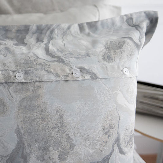 A close-up of a gray Opus | Jacquard sham with a flange and horizontal back button band on a pillow.