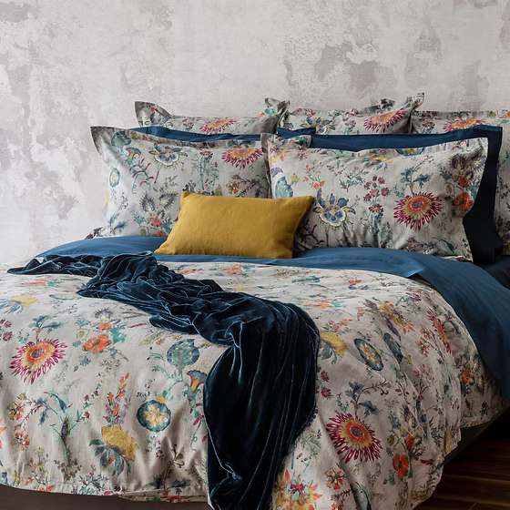 Floral Morgan Printed Sateen bedding set with a blue throw and yellow pillow on a bed against a textured wall.
