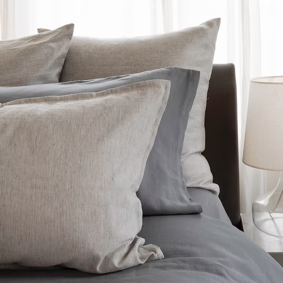 Riva Jacquard pillows in latte and denim on a bed with a lamp in the background