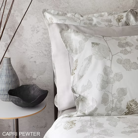 Aspen printed sateen floral patterned pillows on a bed with a side table and decorative items.