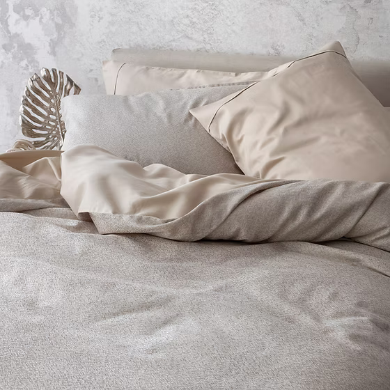 Neatly made bed with Rio | Jacquar Pearl bedding and pillows against a light gray wall.