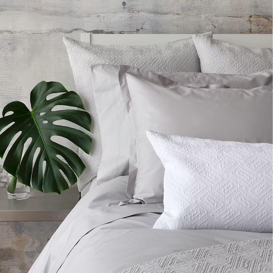 Neatly made bed with textured Scala Matelassé bedding and pillows against a wooden wall.