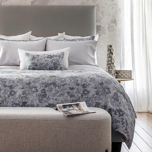 A bed with Sakura jacquard bedding in a gray floral pattern, with a duvet cover and multiple pillows arranged on the bed.