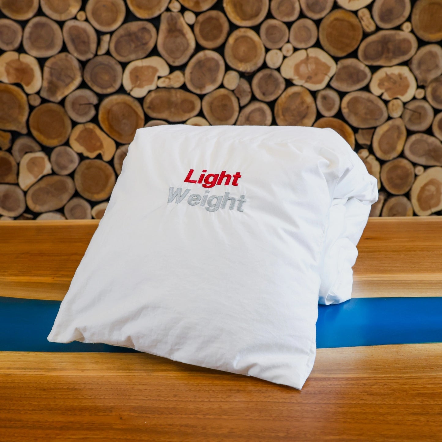 Light weight down duvet folded on a table in front of a wooden wall.