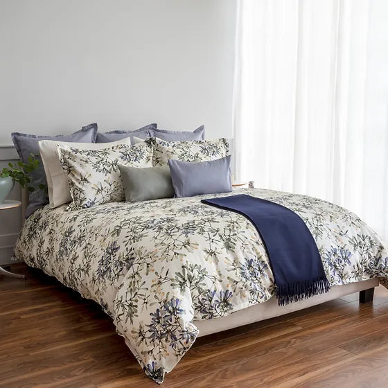 A bed with a Paloma duvet cover set featuring a floral print in modern color schemes, including a pillow with a navy blue cover, placed in a room with a light interior.