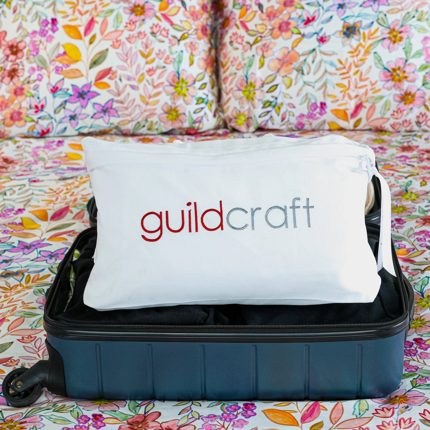 Travel pillow packed in its storage case placed flat in a packed suitcase.