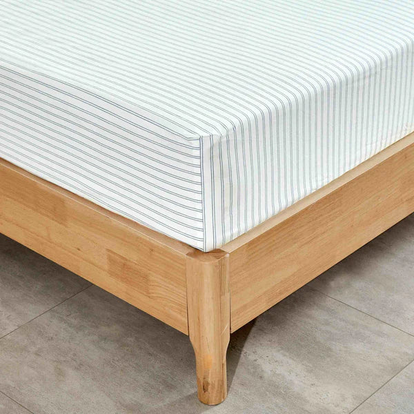 Wooden bed frame with striped Vale Shadow Sheet on a tiled floor