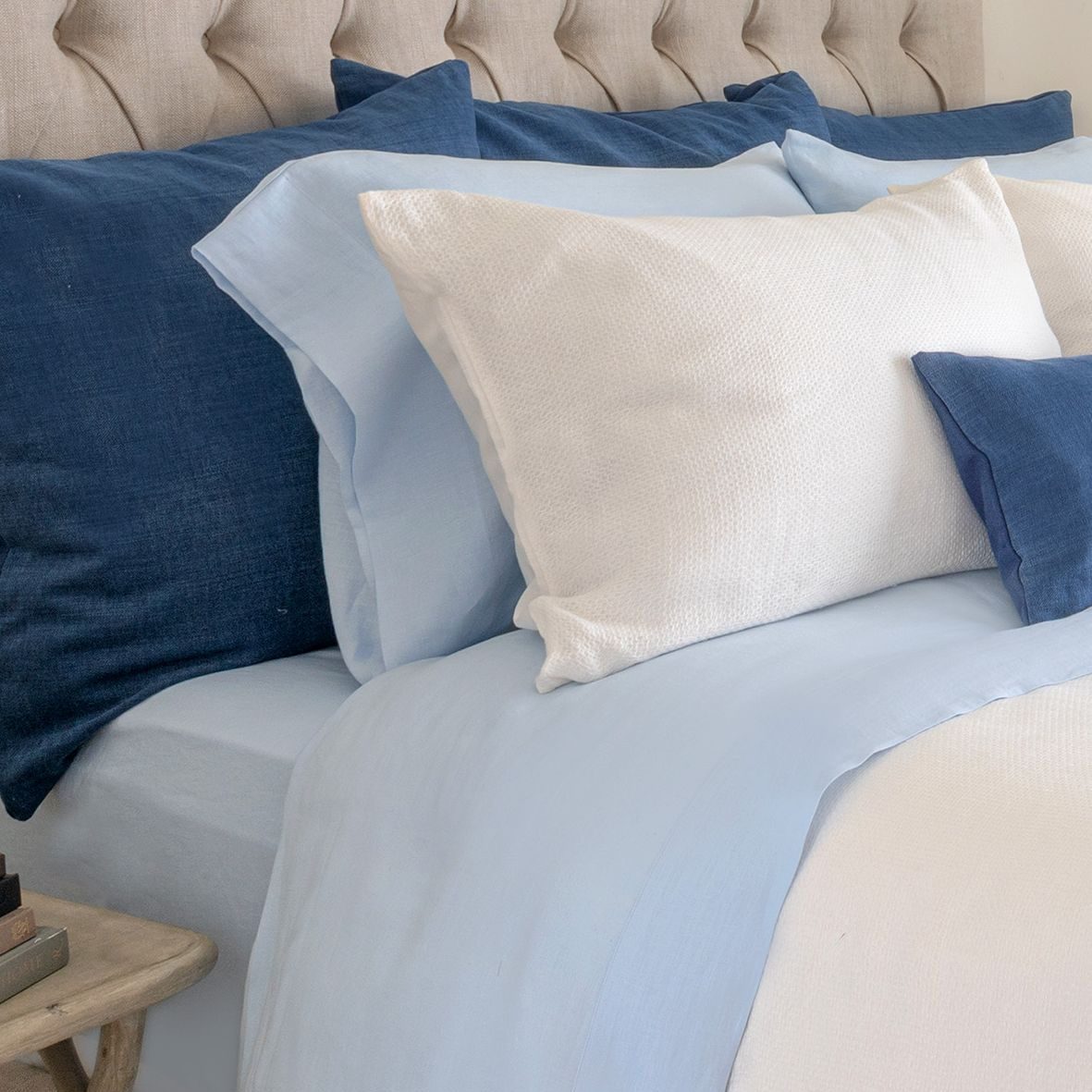 A bed with blue and white Avalon Honeycomb Linen Cushions on a bed, with a decorative pillow behind them.