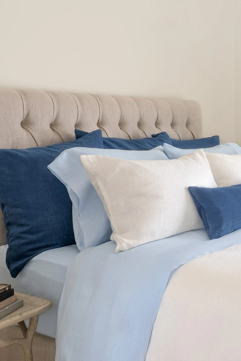 A bed with blue and white Avalon Honeycomb Linen Cushions, including a duvet cover, cushions, and a headboard.