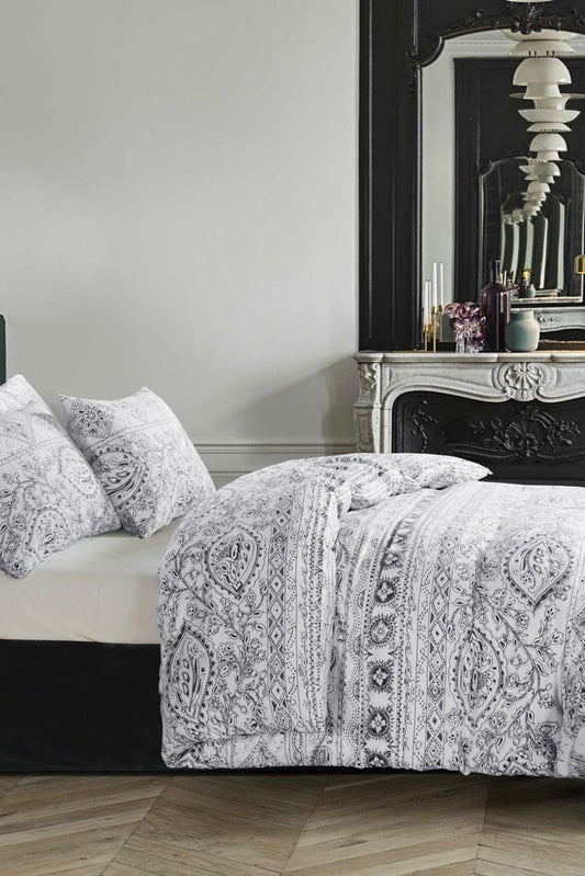 A Riva duvet cover set in a dark navy/grey pattern on a warm white background, displayed on a bed with white pillows.